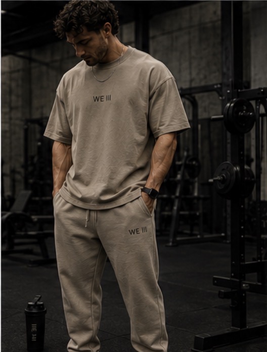 Model wearing the WE III sand oversized tee and sweatpants in a gym